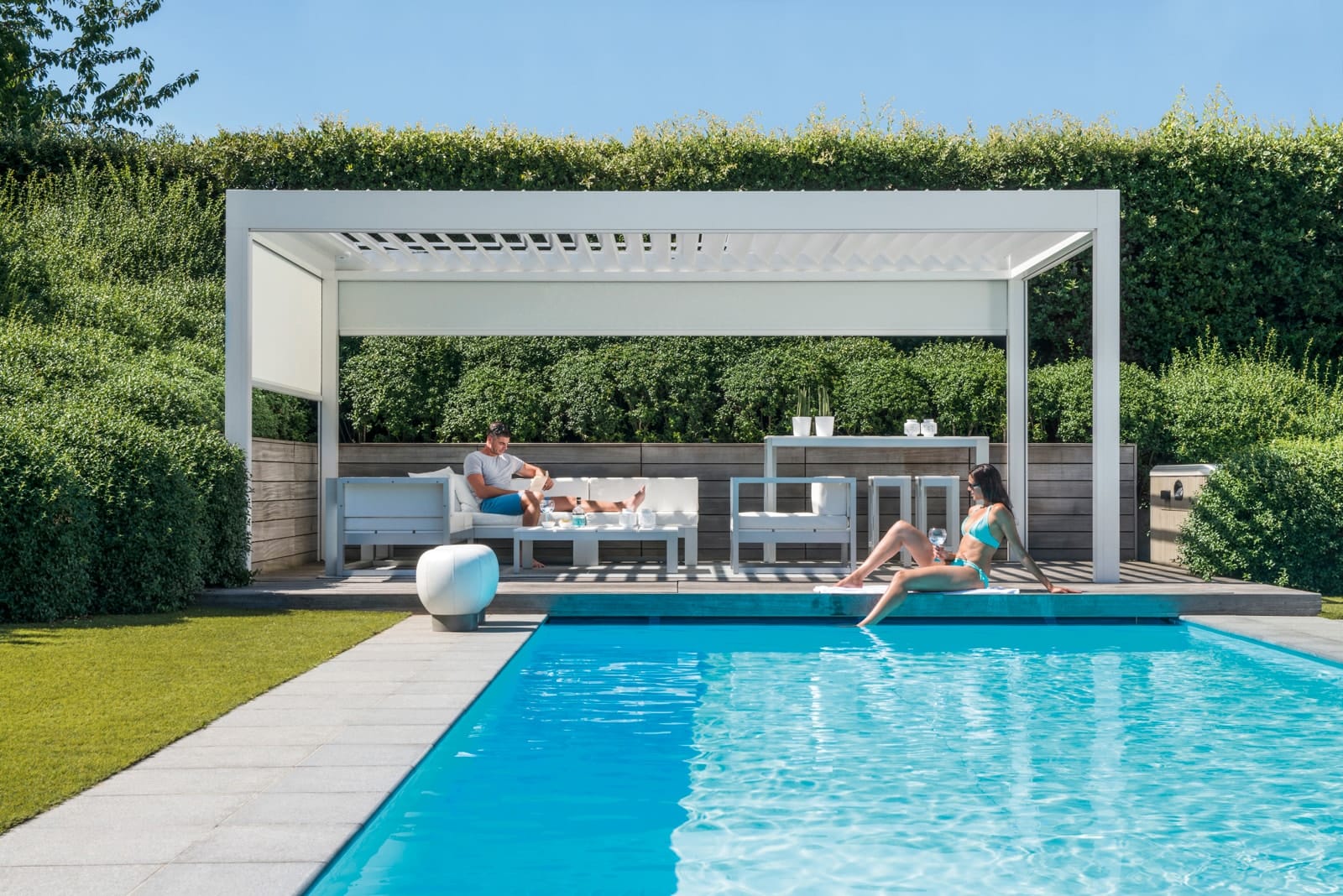 Renson Camargue terrasoverkapping met witte aluminium lamellen boven een lounge terras in een groene tuin
